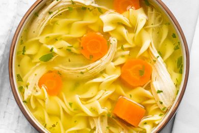 A bowl of chicken noodle soup with egg noodles carrot slices shredded chicken and parsley