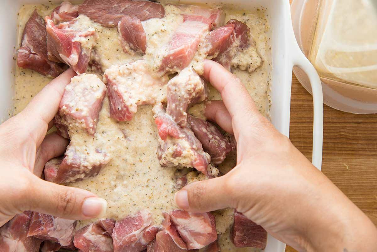 Hands are mixing the pork with the mojo marinade to make garlic and citrus grilled pork kebabs.
