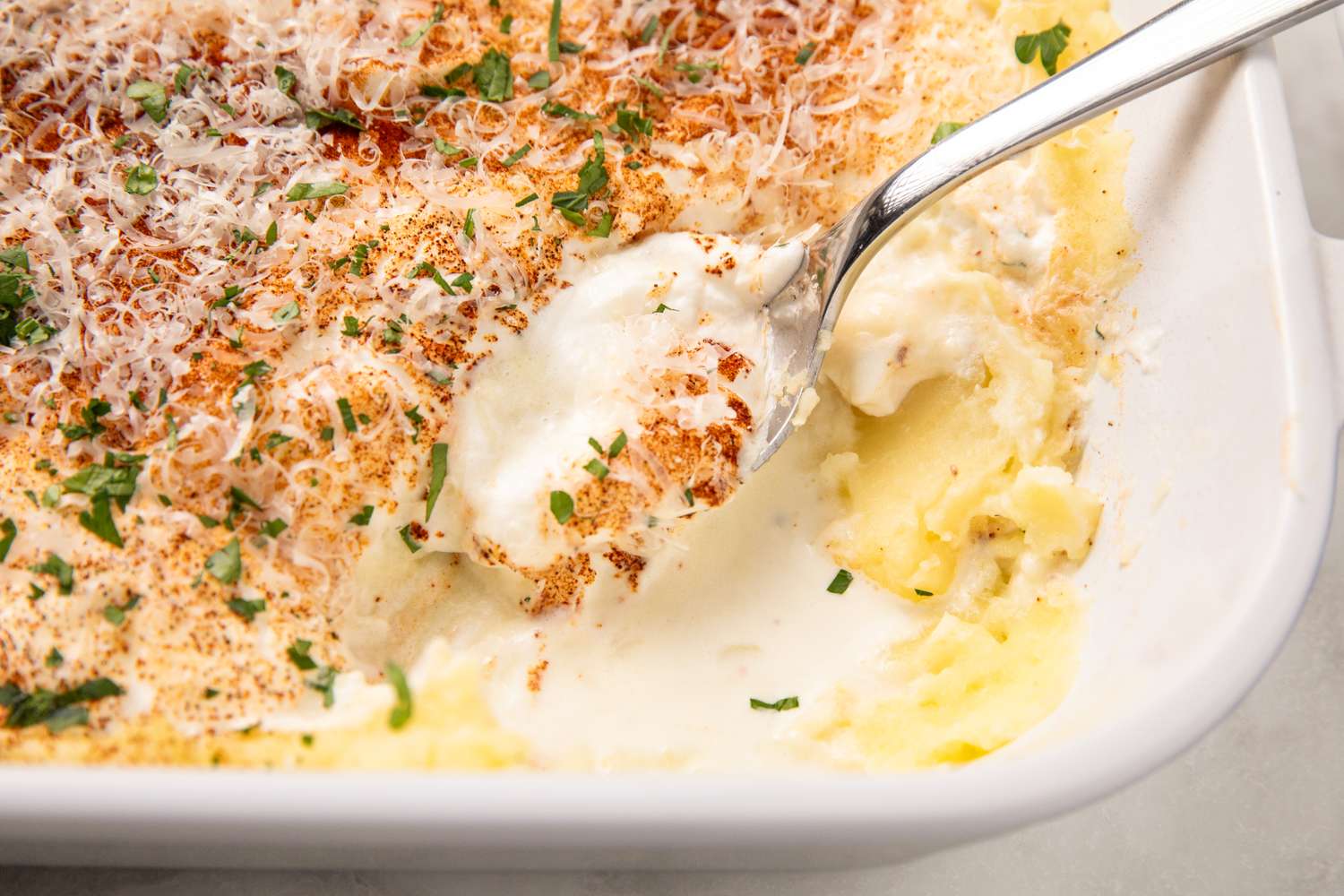 A serving dish containing a casserole with a spoon scooping into it showing a creamy and textured interior