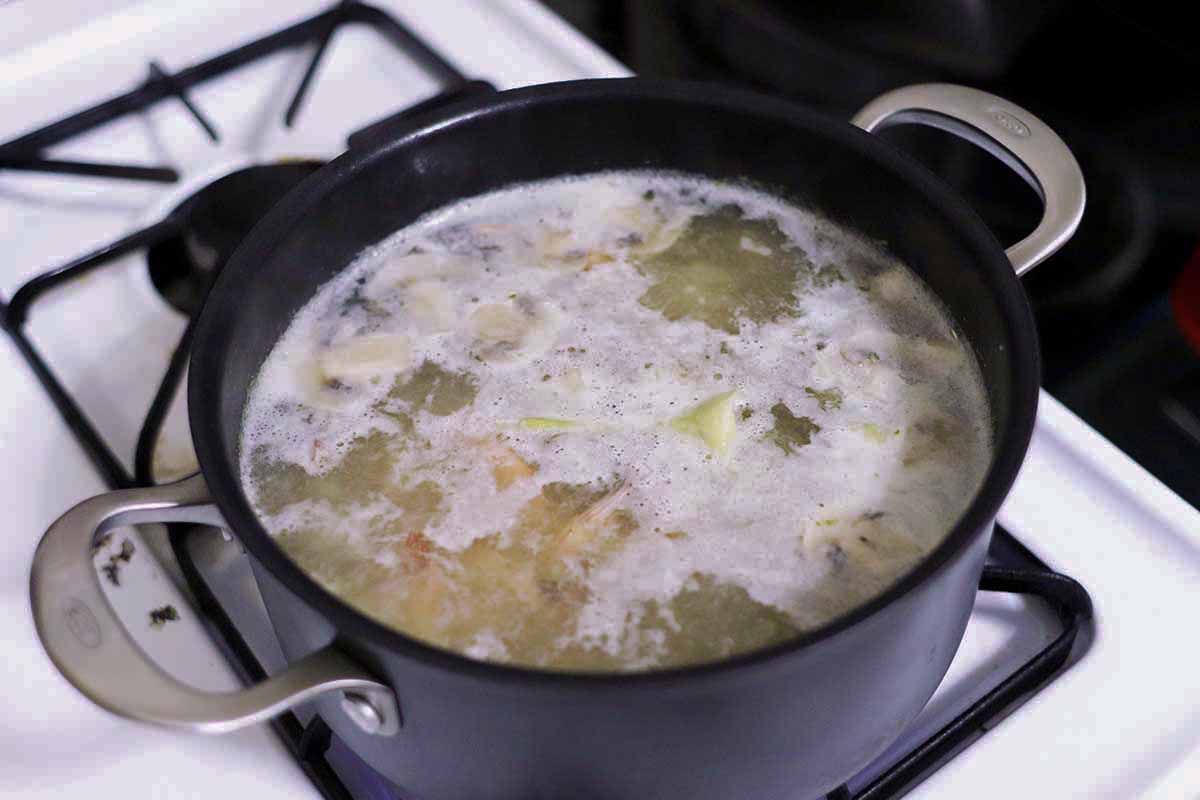 Tom yum soup simmering in a black pot on the stove.