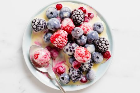 Frozen berries with white chocolate sauce on a plate with a spoon