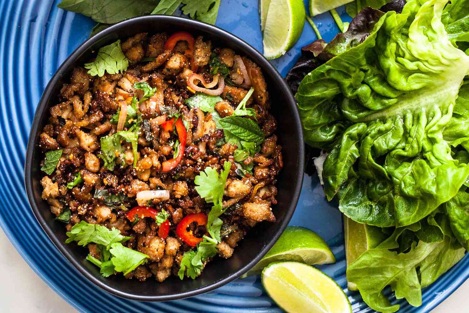 Larb gai in black bowl with lettuce leaves.