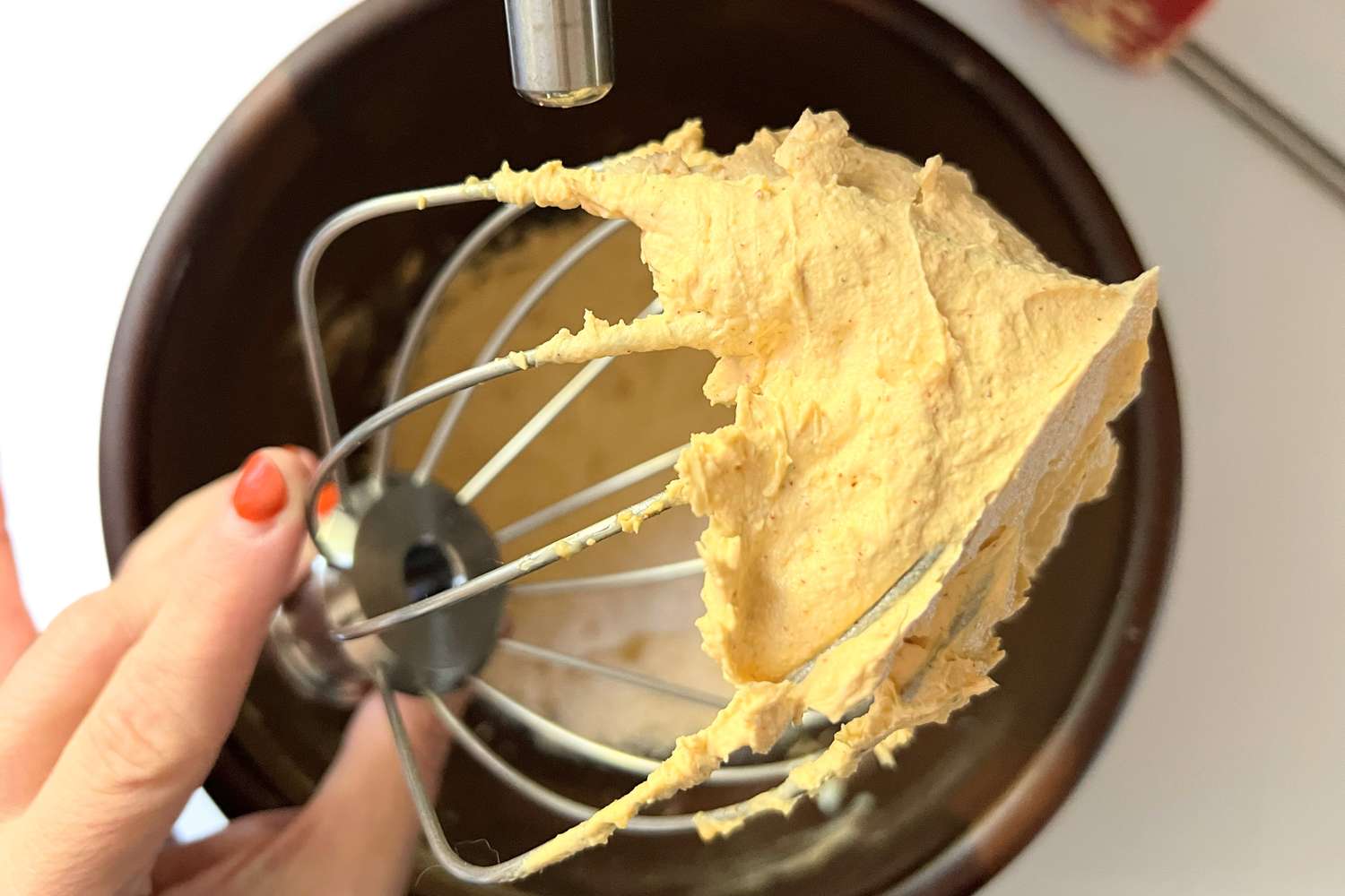 Hand holding a whisk with creamy mixture over a mixing bowl