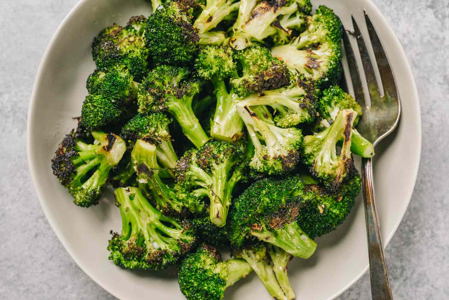 Overhead shot of roasted broccoli on a white plate, with a fork