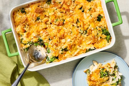 Overhead view of chicken and broccoli casserole in a green dish with a serving spoon next to a small plate with a serving