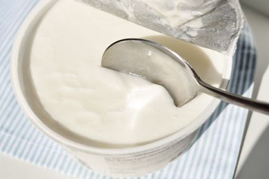 A spoon dipped into a container of yogurt on a striped surface