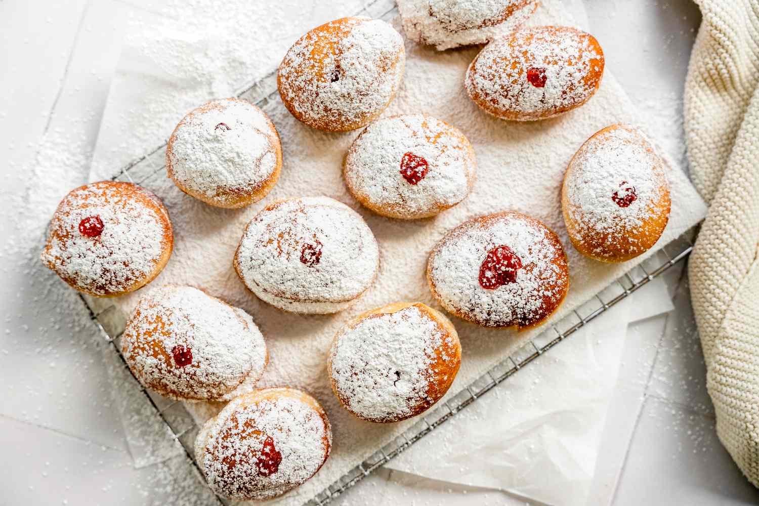 Sufganiyot (Israeli Jelly Donuts) on a Lined Cooling Rack Sitting on Parchment Paper and Next to a Knit Fabric 