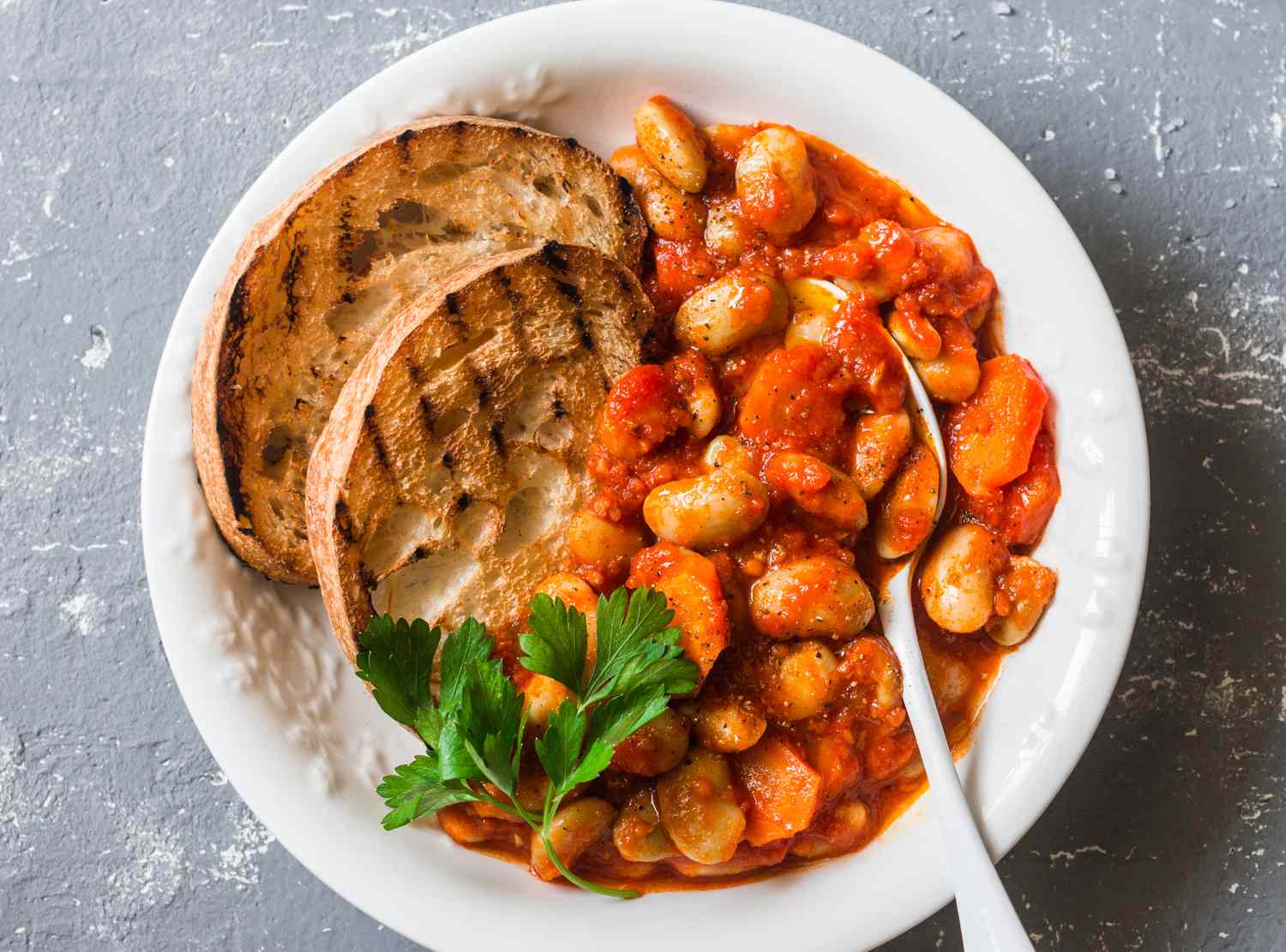 Plate of beans in tomato sauce next to two slices of toasted bread garnished with parsley