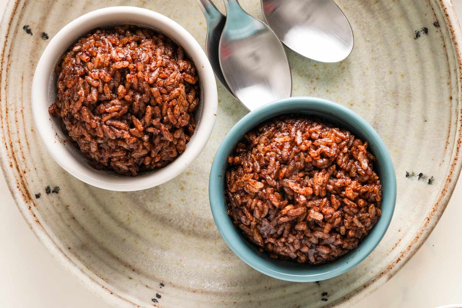 Two bowls of chocolate rice pudding next to spoons on a plate