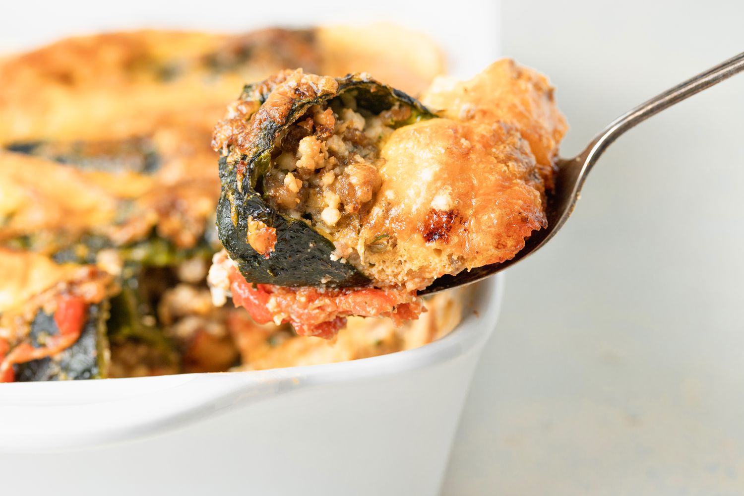 Spooning chili relleno casserole out of a white casserole dish.