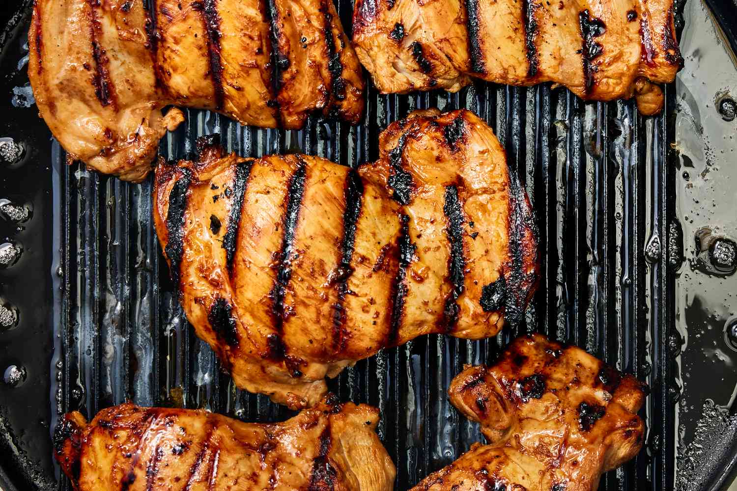 Grilled chicken pieces with charred grill lines on top of a grill pan for Huli Huli Chicken recipe