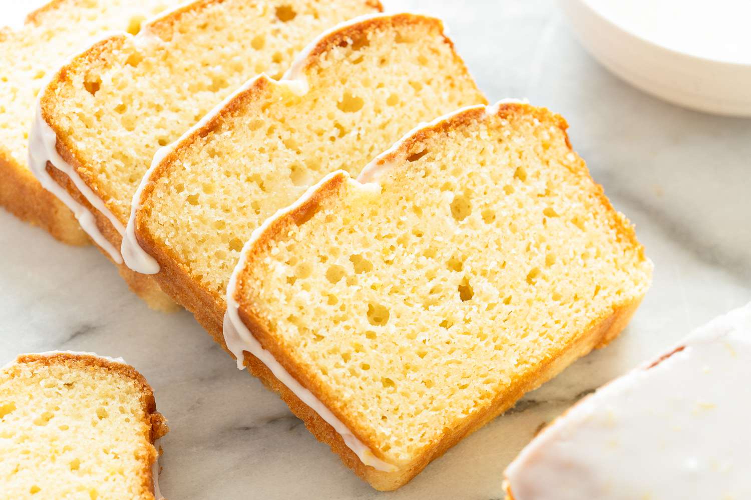 Slices of glazed pound cake on a marble surface.