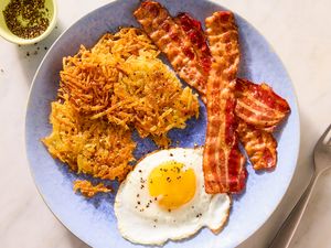 Plate with crispy hash browns sunnysideup egg and strips of cooked bacon