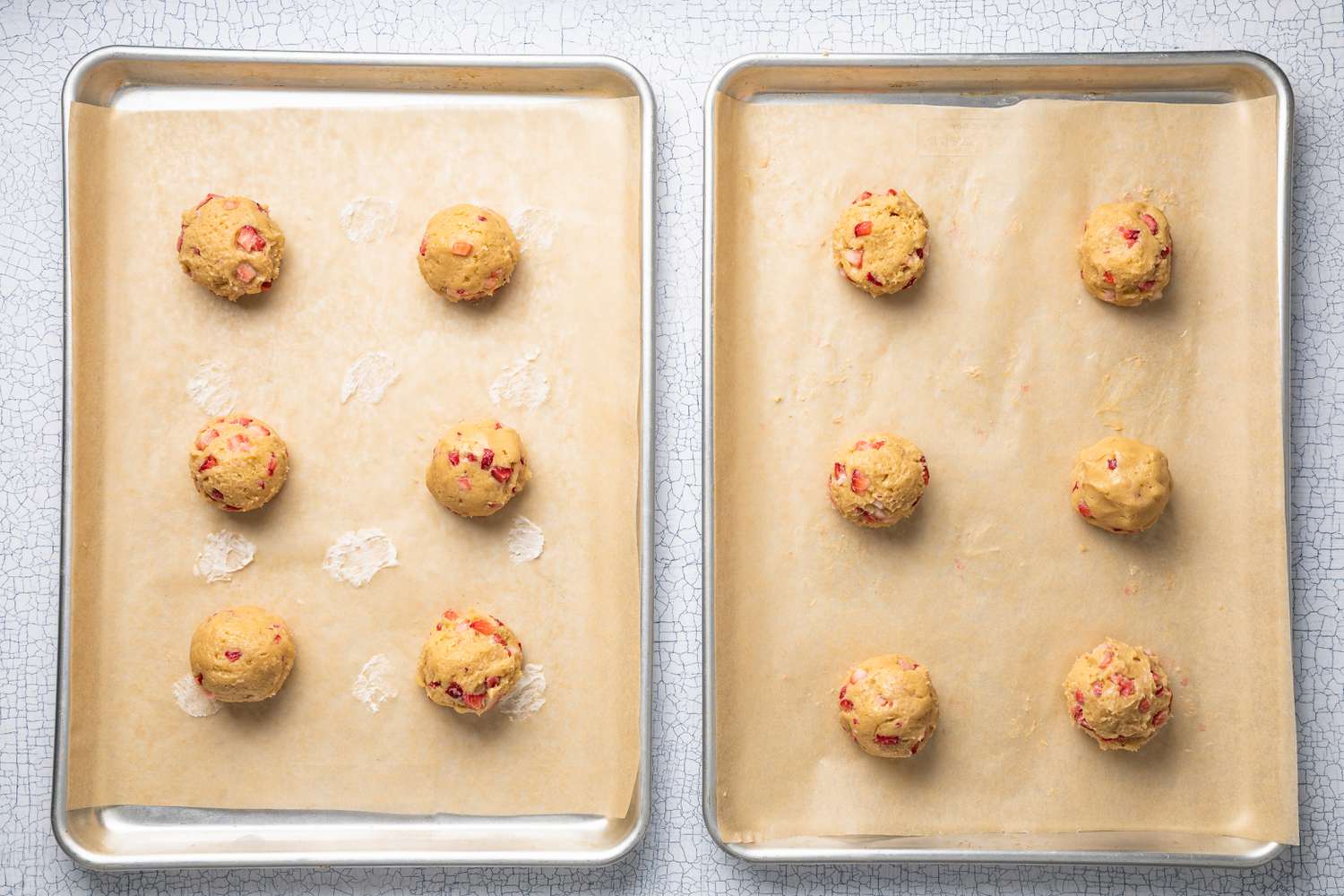 Two Parchment Paper Lined Baking Sheets With 6 Mounds of Strawberry Cheesecake Cookie Dough on Each