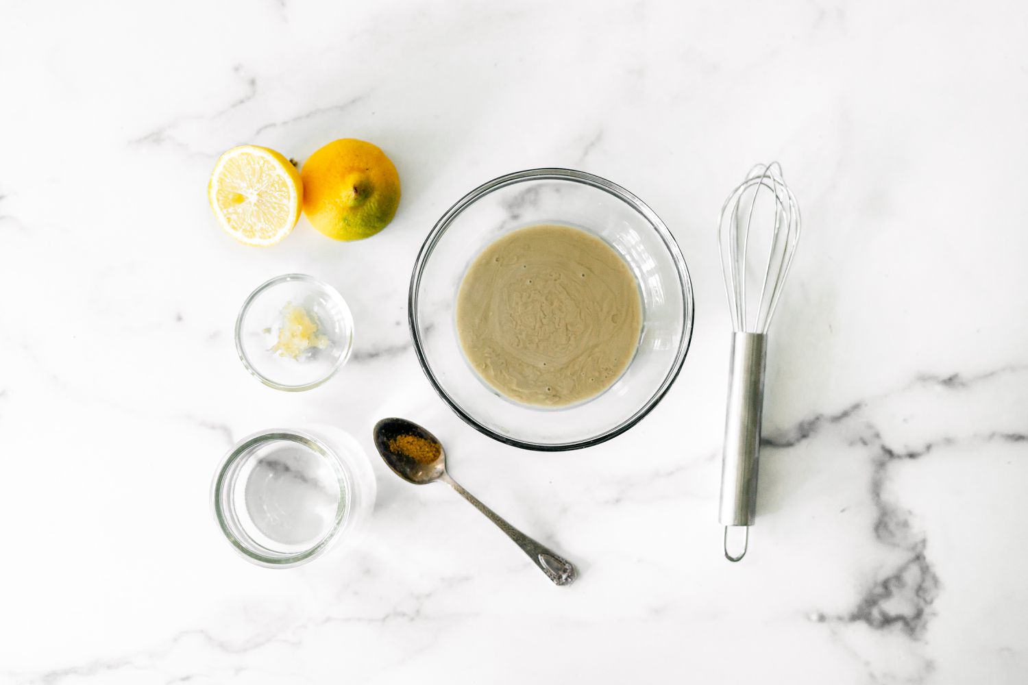 Ingredients for Tahini Sauce (Bowl of Tahini, Small Bowl of Minced Garlic, Halved Lemon, and Spoon of Cumin) for Sabich Recipe