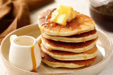 Stack of pancakes with butter and syrup served with a small jug of syrup