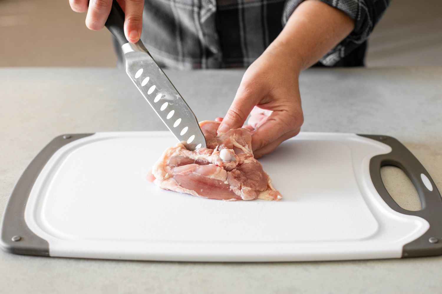 Knife Cutting along the Other Side of the Bone While the Other Hand Holds the Chicken Thigh