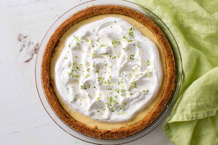 Overhead shot of a homemade keylime pie, covered with whipped cream and with a linen beside