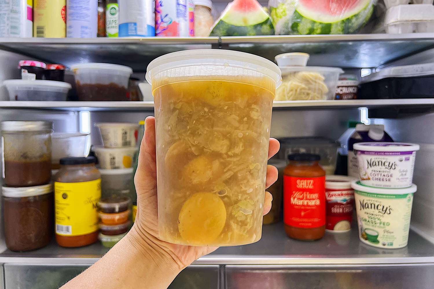 hand holding 4-Ingredient Cabbage and Potato Soup in a container in front of an open refrigerator