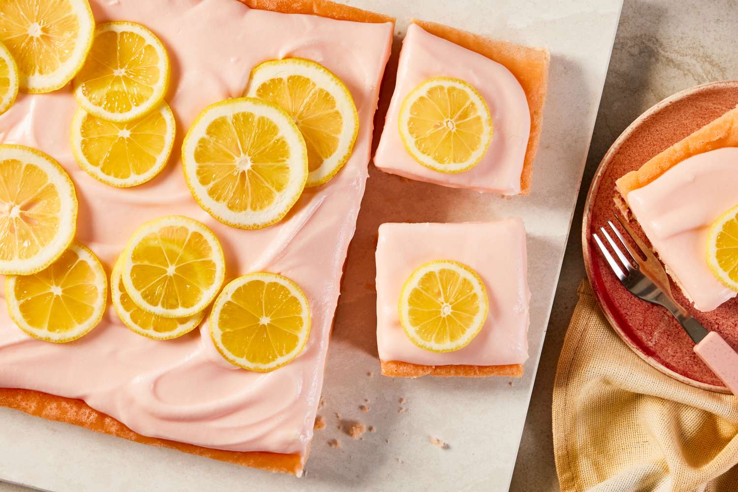 pink lemonade cake (with some slices cut out) on a board next to a plate with a slice 