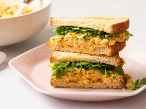 Angled view of curried chickpea salad sandwich on a pink plate, all on a white background