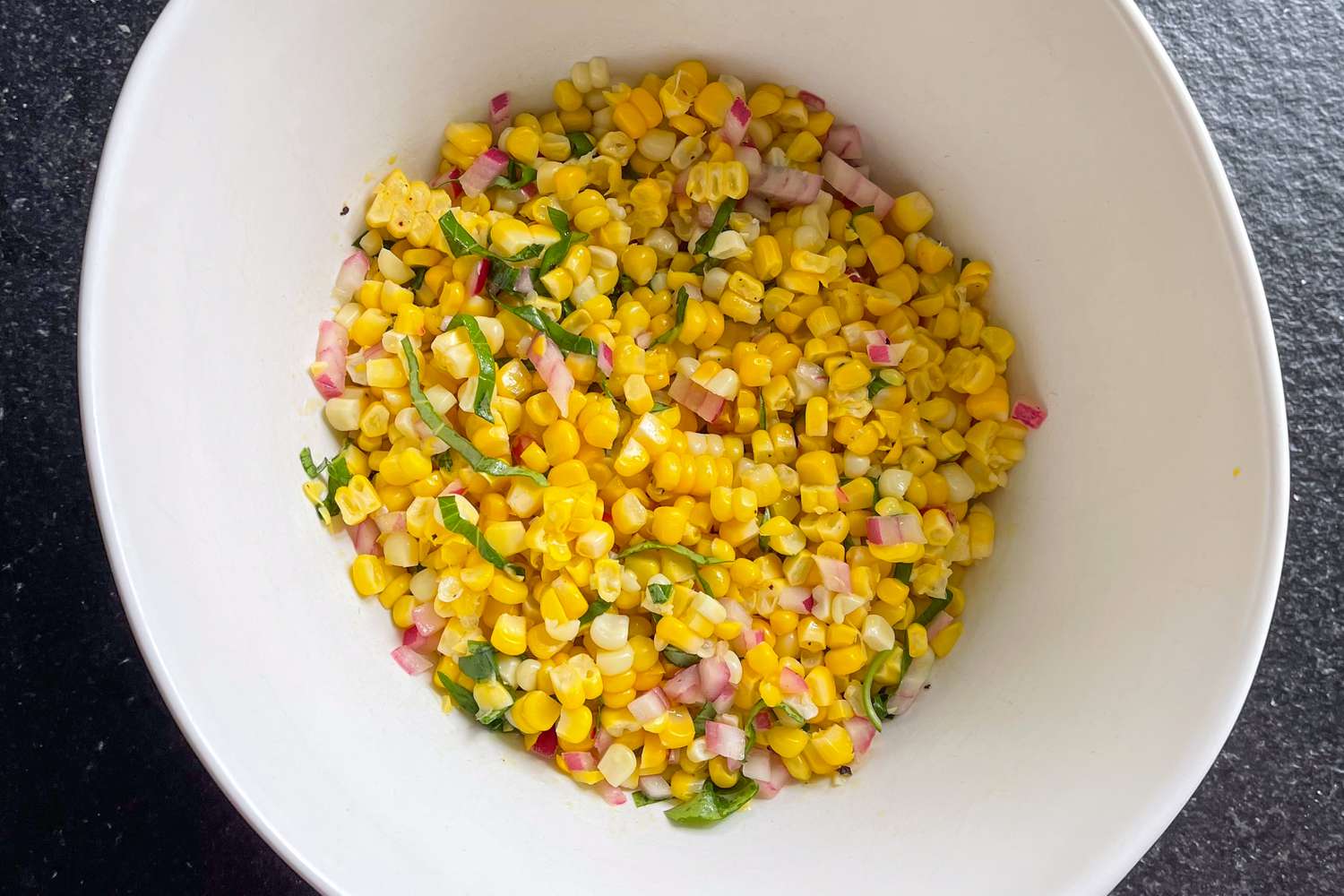 Ina Garten's fresh corn salad in a white bowl showing ribbons of basil and minced red onion