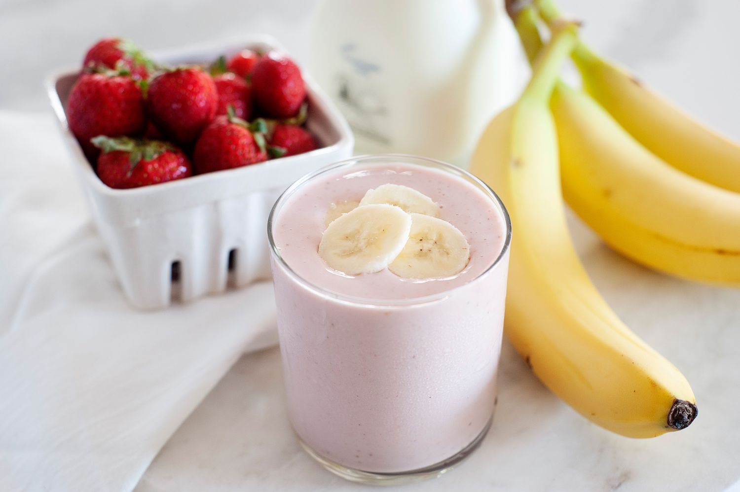 Quick and easy strawberry banana smoothie garnished with sliced bananas and with whole fruit set around it.
