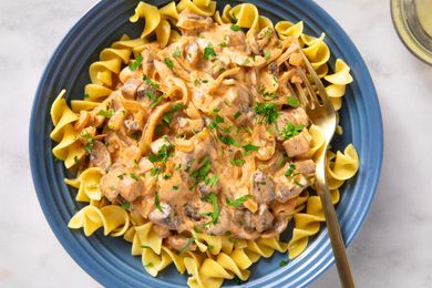 A plate of mushroom stroganoff served over egg noodles garnished with parsley with a fork on the side