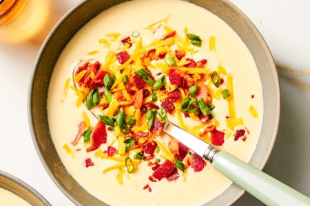 Bowl of loaded potato soup garnished with shredded cheese scallions and bacon with a spoon