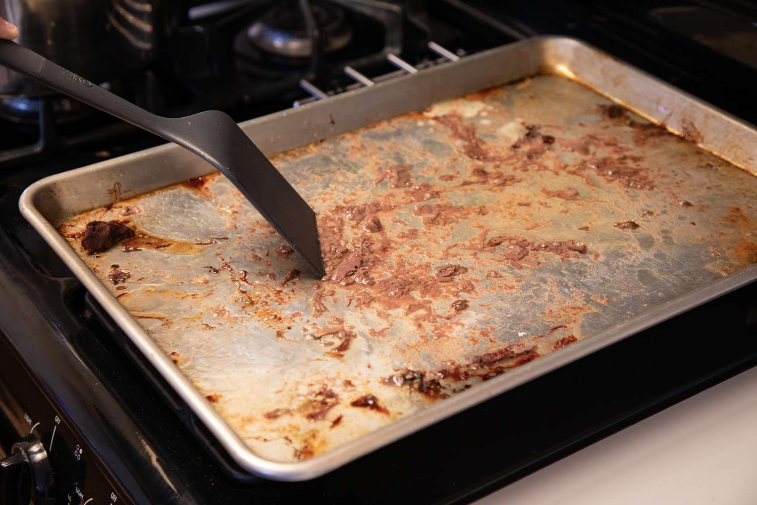 Scraping the drippings off a baking sheet to make a beef broth recipe.