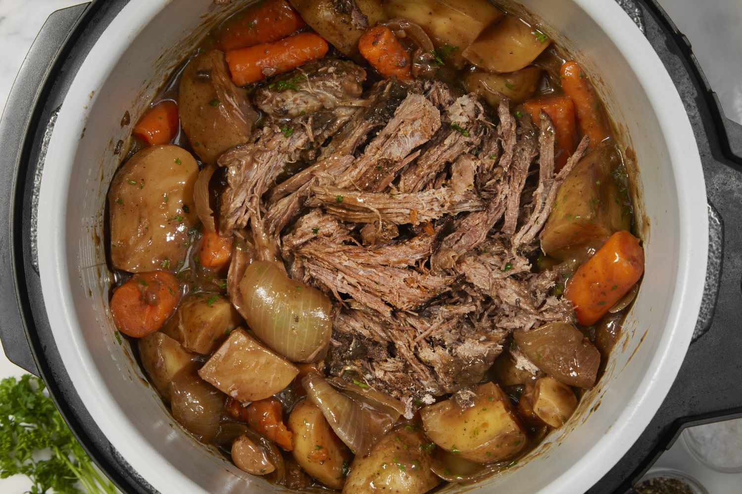 Slow cooker with shredded beef carrots potatoes and onions in a broth