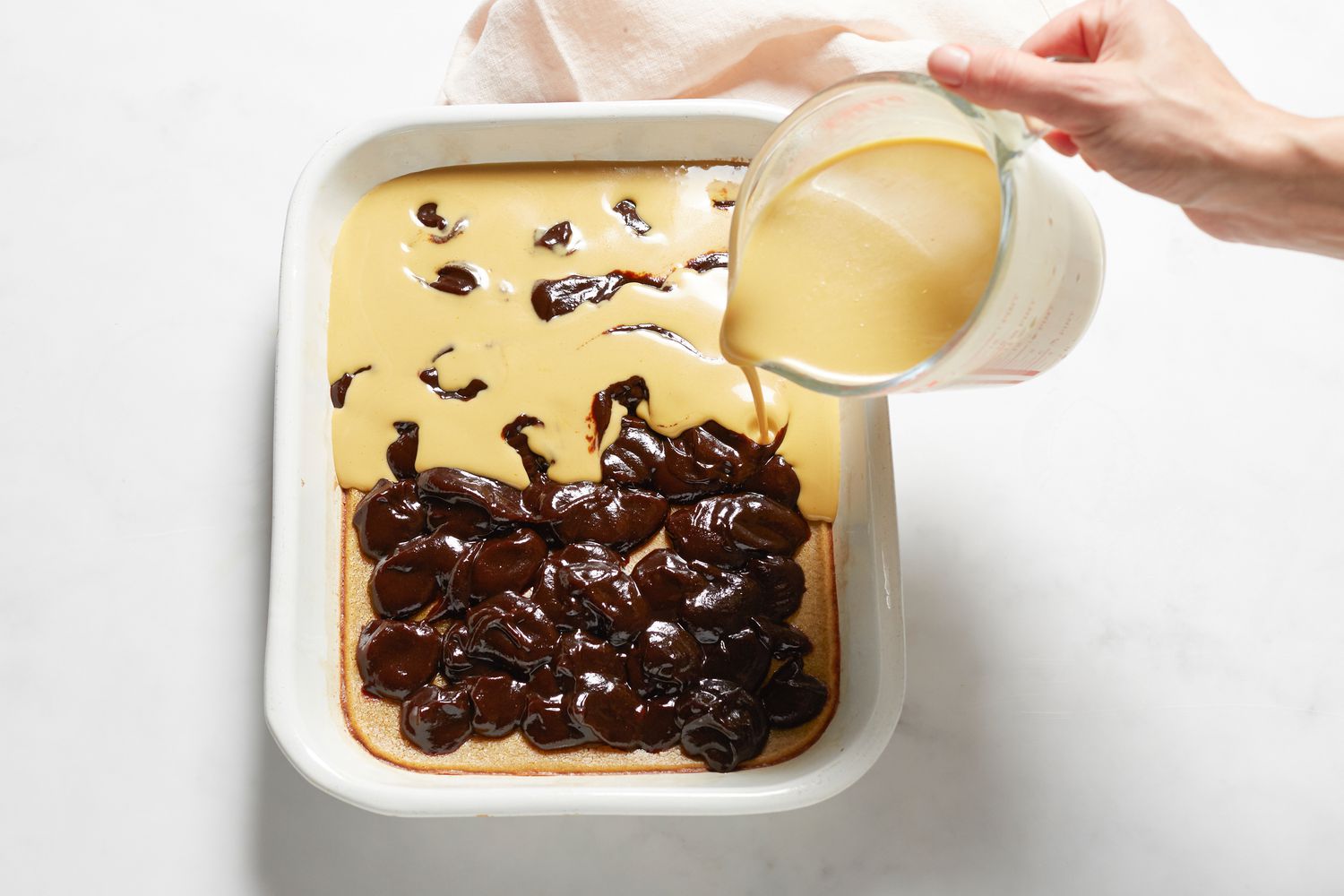 Pouring batter and spreading bean paste on a Sticky rice cake with red bean paste in a baking dish.