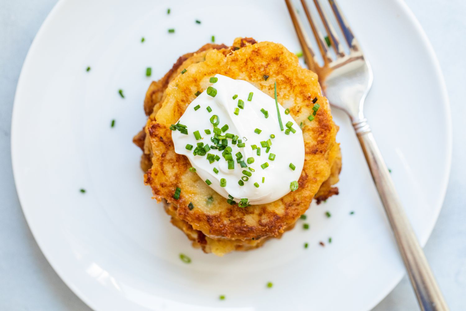 Overhead view of Potato Pancakes made with leftover mashed potatoes stacked on a plate and topped with sour cream.