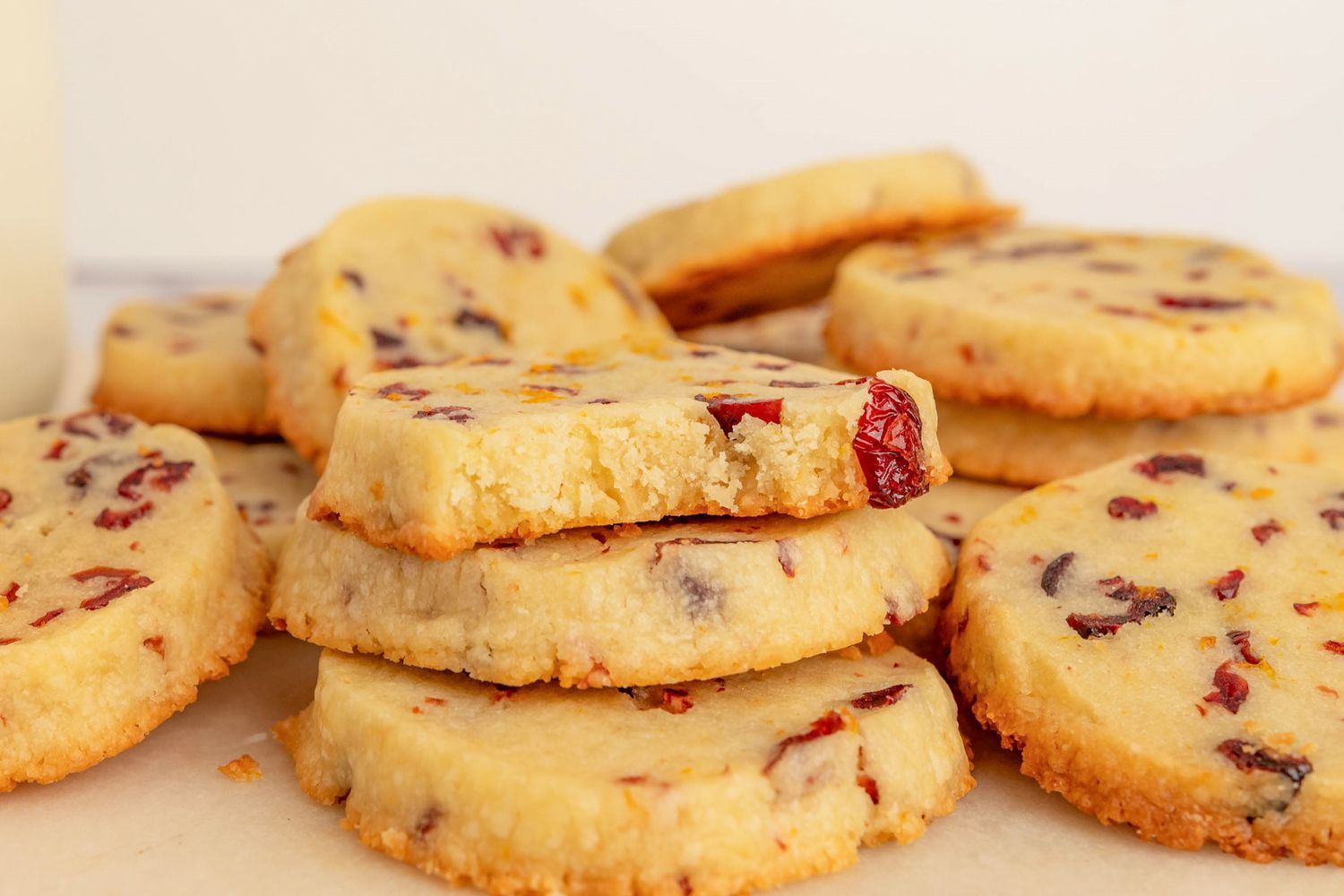 Side view of a stack of three cranberry orange shortbread cookies with more in the background