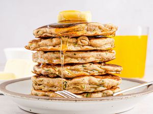 A tall stack of sweet zucchini pancakes on a plate with butter and syrup on top