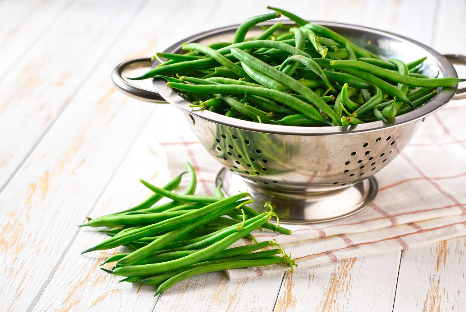 Side view of green beans in a colander on a white table