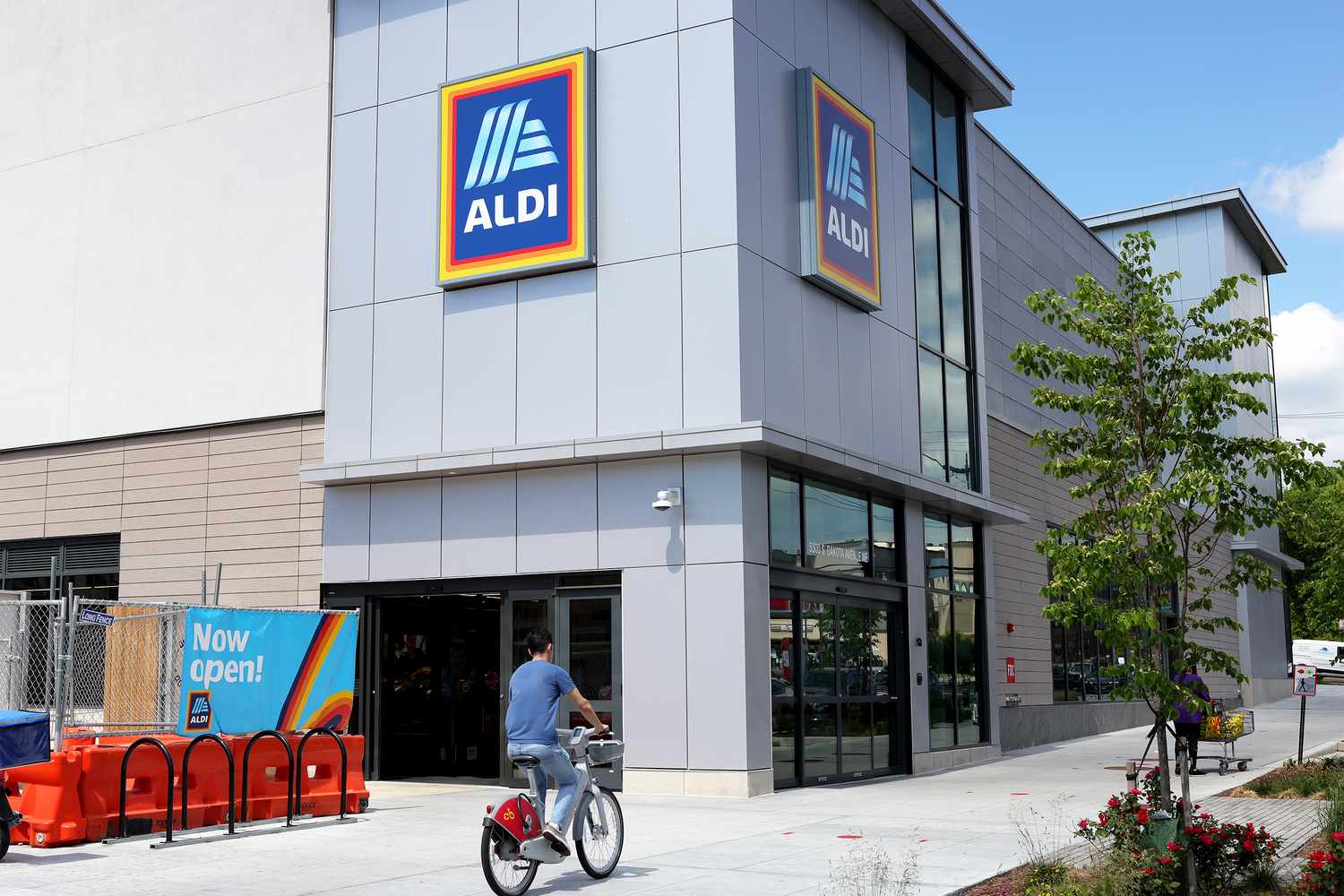 Exterior of an ALDI grocery store with a pedestrian riding a bicycle past the entrance