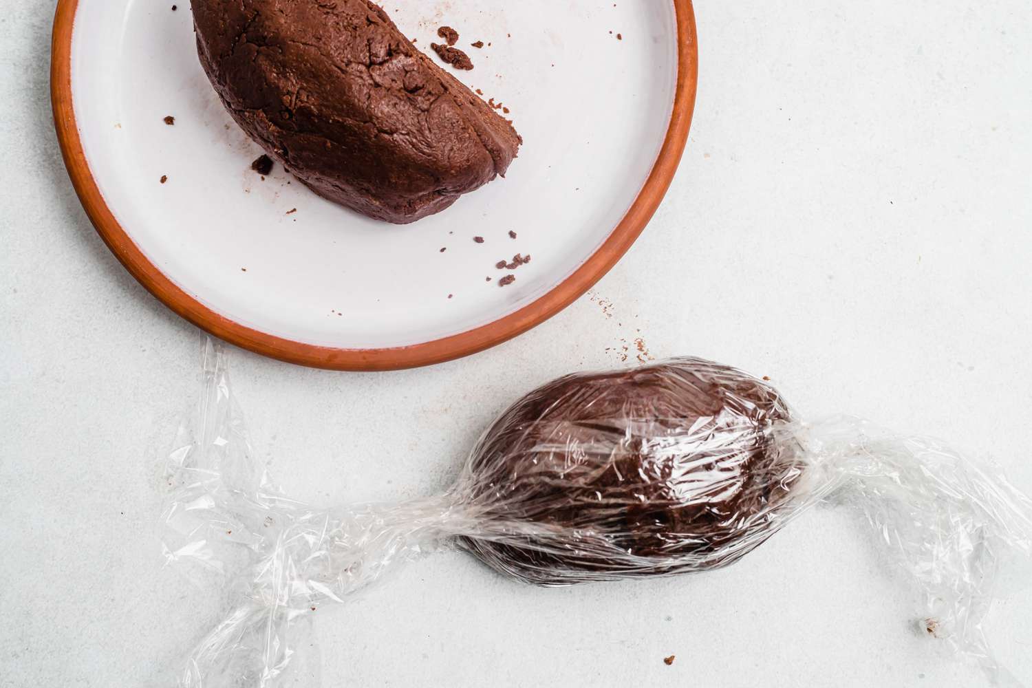 Chocolate dough split half with one half wrapped in plastic wrap.