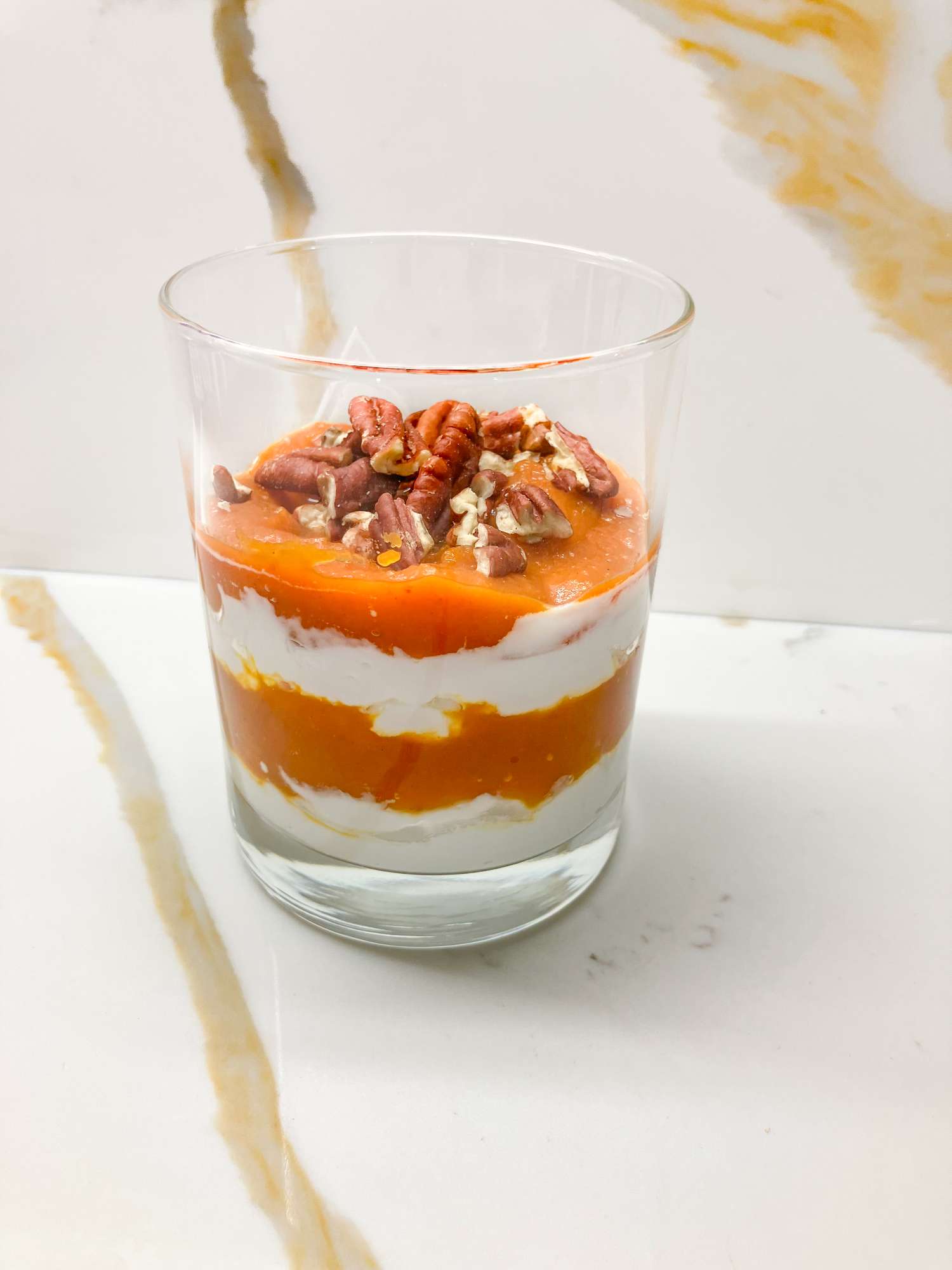 Glass of layered dessert with cream pumpkin puree and pecans on a marble surface