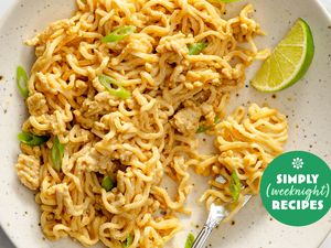Plate of noodles garnished with green onions and a lime wedge fork resting on the plate