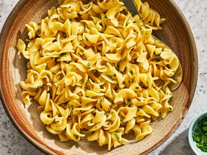 A bowl of buttered noodles garnished with herbs with a small dish of garnishes on the side