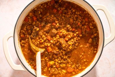 A pot of beef barley soup with visible chunks of meat and vegetables and a wooden spoon