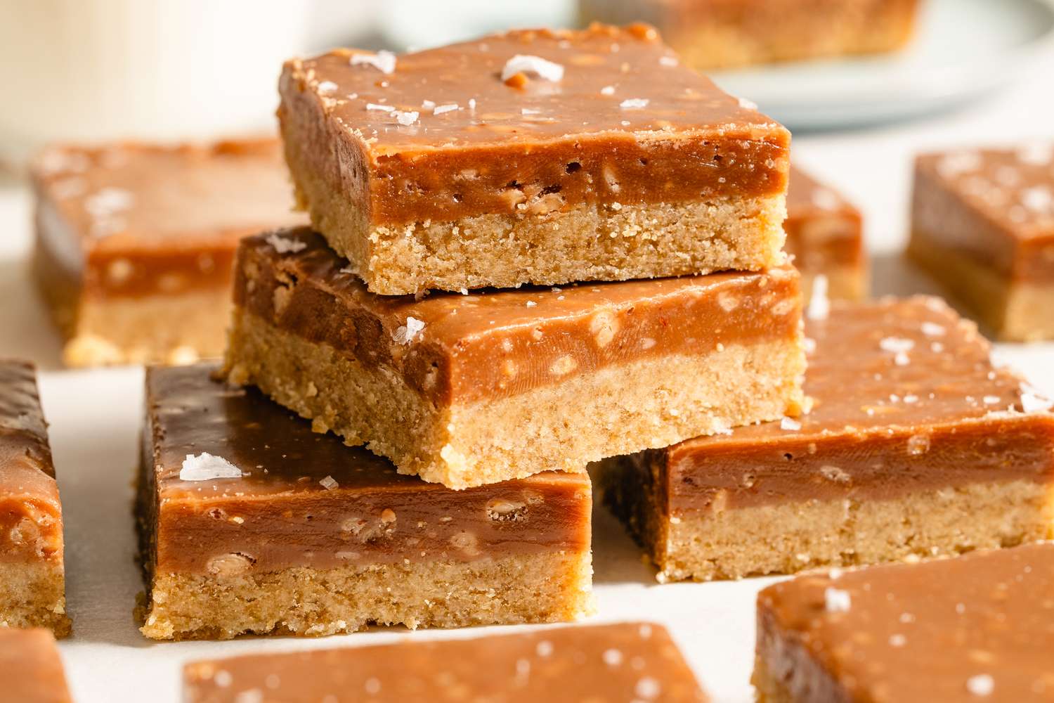 Stacked caramel dessert squares on a white surface with additional squares around