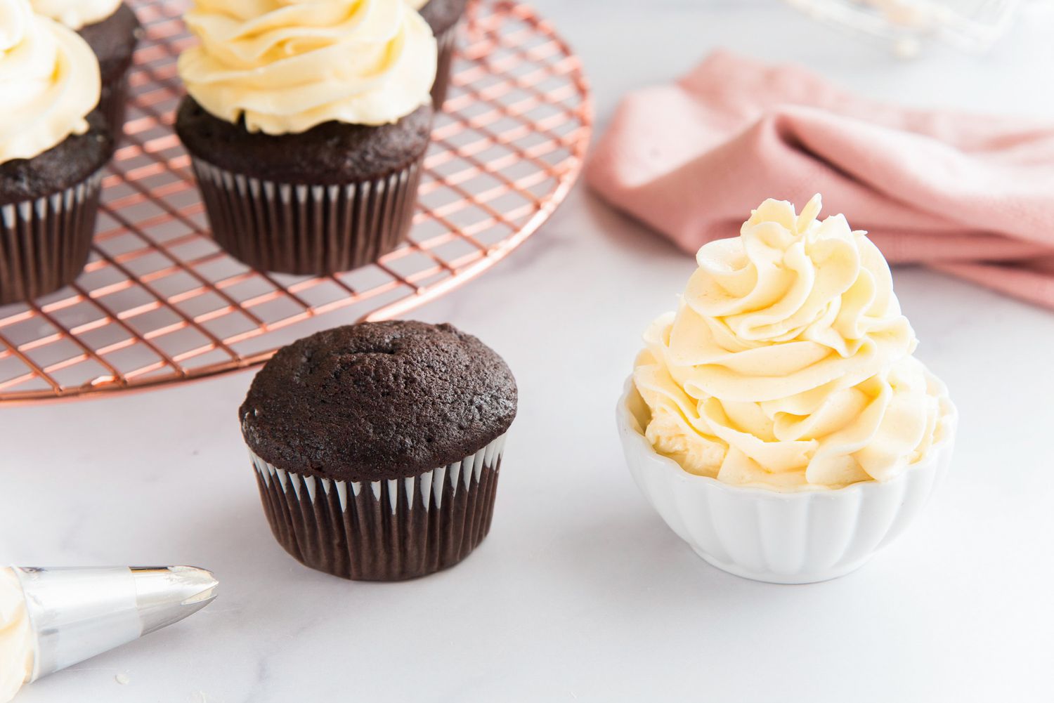 The best French buttercream piped in a small bowl and chocolate cupcakes to the left.