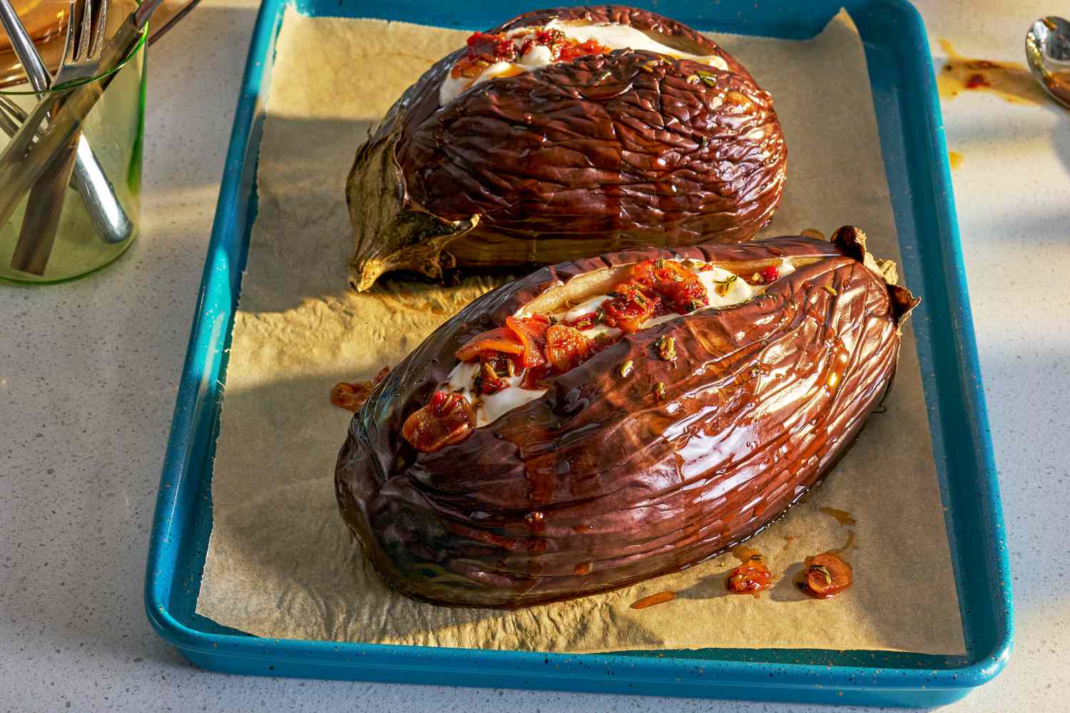 Two whole roasted eggplant on a baking sheet, topped with yogurt and chili crisp