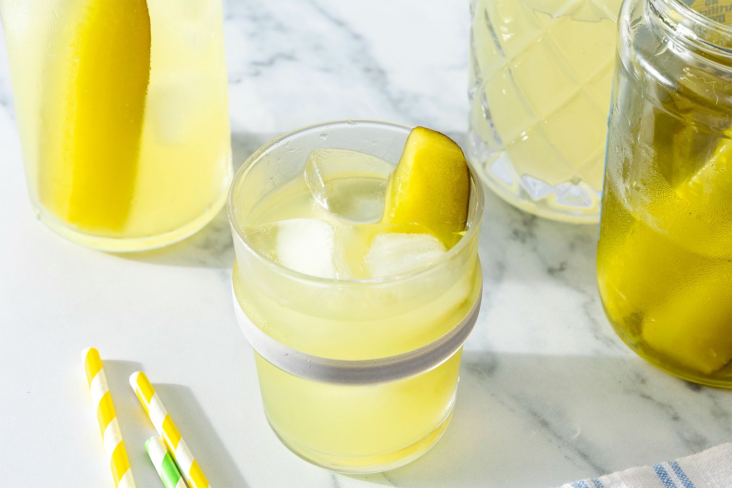 Pickle Lemonade in a cocktail glass garnished with a pickle spear, jar of pickle spears, extra straws