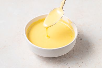 Blender Hollandaise Sauce in a white bowl with sauce dripping off of a spoon.