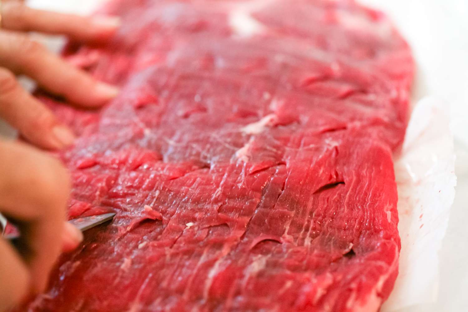 Cutting slits in raw flank steak.