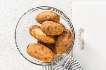 A bowl of russet potatoes on a counter next to a cutting board and cloth