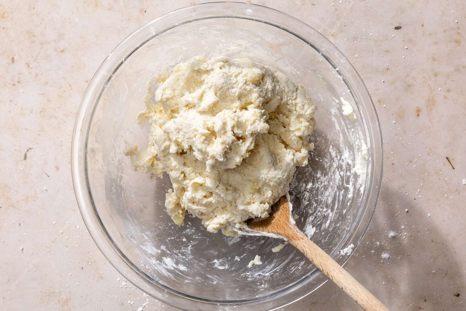 Overhead view of a clear glass bowl of the dry and wet ingredients being mixed with a wooden spoon for Mashed Potato Biscuits recipe